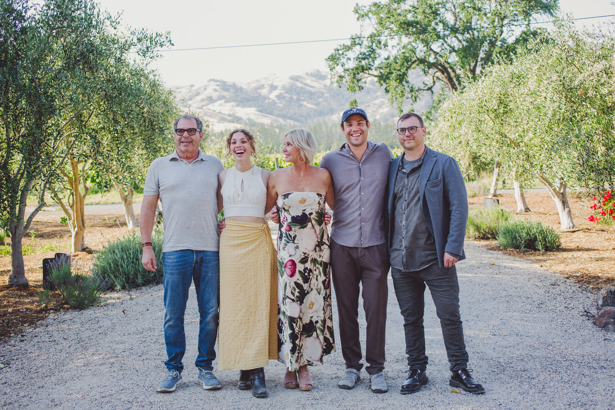 The Ehret Family standing together outdoors on a gravel path with trees and hills in the background.